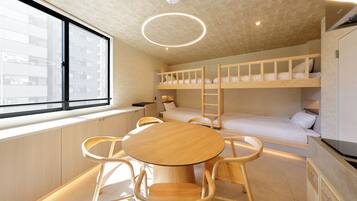 Ein modernes Zimmer mit Etagenbetten, einem runden Holztisch, Stühlen, einem großen Fenster und einer runden Leuchte.