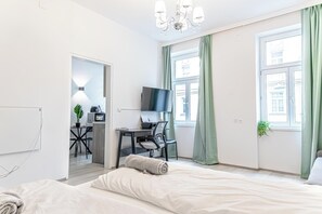A modern hotel room with a bed, a desk with a computer, a TV, and a view of the city through large windows. - Modern Apt Near Praterstern & Danube (Vienna)