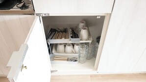 Une cuisine avec des meubles blancs, un plan de travail en bois et un tiroir contenant des ustensiles de cuisine et de la verrerie.