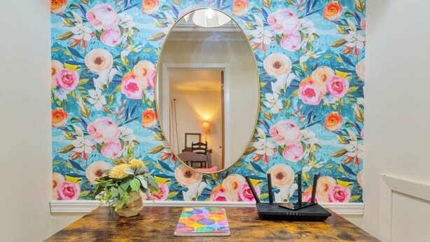 Een kamer met een houten tafel, een spiegel en bloemenbehang.