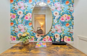A room with a wooden table, a mirror, and a floral wallpaper.
