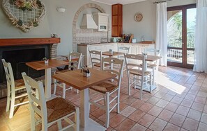 Ein Essbereich mit weißen Stühlen und Tischen, einem Kamin, einer Küche mit weißen Schränken und Blick durch eine Glastür.