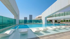 A rooftop pool with clear glass walls, modern white lounge chairs, and a view of city skyscrapers. - Vogue | Al Wasl 1 Residence near World Trade Centre (Dubai)