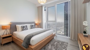 A modern bedroom with a large bed, a nightstand, a lamp, a view of the city through the window, and a small table with a plant. - Vogue | Al Wasl 1 Residence near World Trade Centre (Dubai)