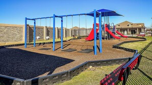 Un parque infantil con columpios, toboganes y una zona vallada.