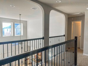 Un intérieur spacieux avec un plafond haut, un escalier doté d’une rampe noire et une vue sur l’extérieur par une fenêtre.