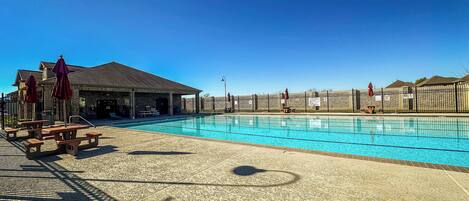 Une piscine dotée d’un pavillon abrité, de tables de pique-nique et d’une zone délimitée par une clôture.