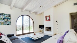 A living room with a large arched window, a flat-screen TV, a fireplace, and a modern sofa. - Luxurious home in Trequanda with outdoor swimming pool (Trequanda)