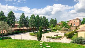 A courtyard with a gravel path, surrounded by trees and buildings with red-tiled roofs. - Luxurious home in Trequanda with outdoor swimming pool (Trequanda)