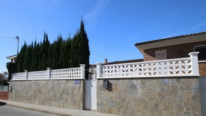 Un mur de pierres avec une clôture en treillis blanche, un ciel dégagé et un bâtiment avec un toit en tuiles.