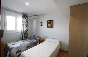Une chambre avec deux lits, une fenêtre avec des rideaux, un climatiseur, un tableau au mur et une armoire en bois.
