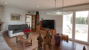 Un salon comprenant un canapé, une table basse, un téléviseur et un coin repas avec des chaises et un vase.