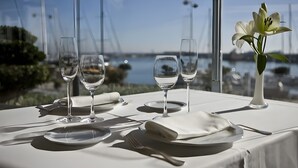 Une table dressée pour le dîner, avec vue sur un plan d’eau et un pont en arrière-plan.