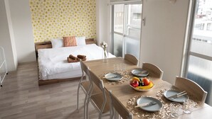 Quarto de hotel com uma cama, uma mesa de jantar posta para dois e uma janela com vista para edifícios.