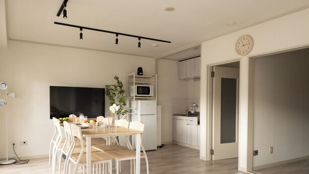 Quarto moderno e bem iluminado, com uma cama, área de refeições com mesa e cadeiras, cozinha equipada com micro-ondas e armários, e uma janela grande.