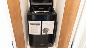 Máquina de lavar compacta e preta num espaço pequeno, com moldura de porta de madeira.