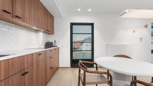 Cozinha moderna com armários de madeira, bancada branca e área de refeições com mesa e cadeiras brancas.