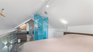 Quarto moderno com uma cama grande, escada de vidro e banheiro com box de vidro.