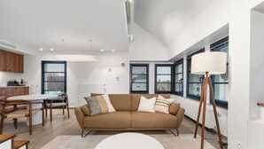 Uma sala de estar moderna com um sofá castanho, mesa de centro branca e mesa de jantar de madeira.
