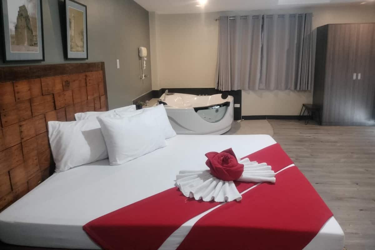 Ein Hotelzimmer mit einem hölzernen Kopfteil, einem Bett mit weißer Bettwäsche, einer rot-weißen Tagesdecke und einer weißen Badewanne.