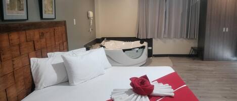 Camera d'albergo con una testiera in legno, un letto con biancheria da letto bianca, una coperta a letto rossa e bianca e una vasca da bagno bianca.