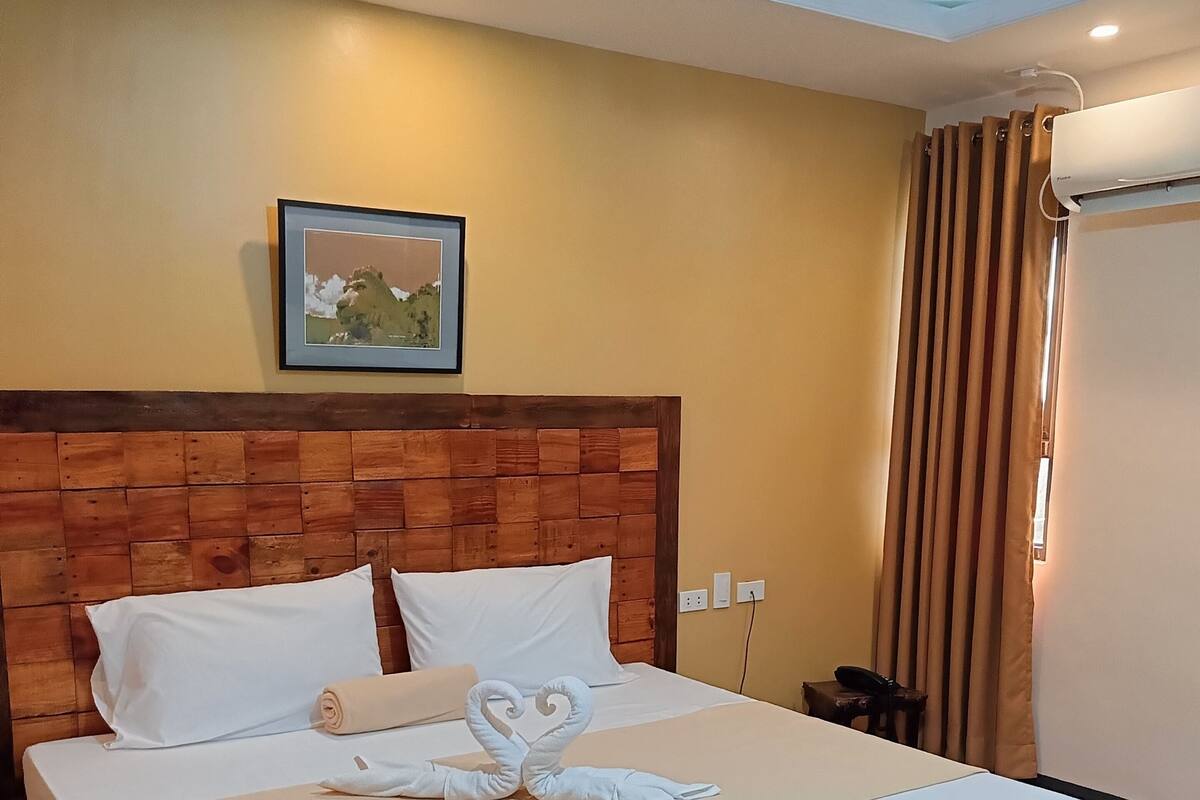 Ein ordentlich bezogenes Bett mit einer herzförmigen Handtuchgestaltung, einem Holz-Kopfteil und einem gerahmten Bild an der Wand.