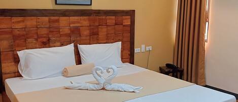 A neatly made bed with a heart-shaped towel arrangement, a wooden headboard, and a framed picture on the wall.