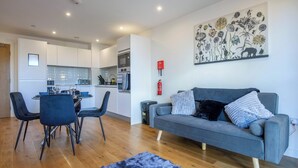 A modern living room with a grey sofa, a dining table with chairs, and a kitchen in the background. - A classy, cozy & modern apartment in Birmingham City centre. (Birmingham)