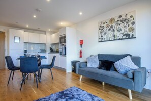 A modern living room with a grey sofa, a dining table with chairs, and a kitchen in the background. - A classy, cozy & modern apartment in Birmingham City centre. (Birmingham)