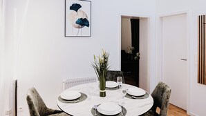 A dining area with a round table, four upholstered chairs, and a framed artwork on the wall.