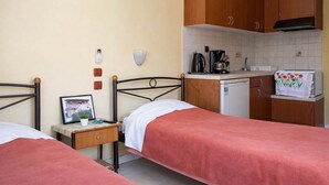 A bedroom with two beds, a small bedside table with a picture frame, a nightstand, and a kitchenette with a coffee maker, kettle, and toaster.