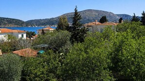 A coastal village with terracotta-roofed houses, a mountain in the background, and a clear blue sea.