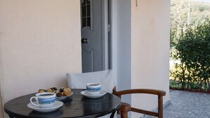 A small round table with two cups and a plate of cookies, a wooden chair, and a window with a door.