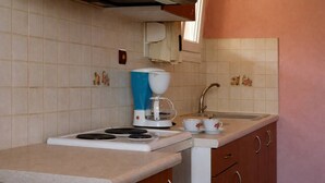 Una cuina compacta amb fogó a gas, cafetera, rentapesos i armaris de fusta.