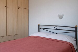 A bed with a metal frame and a red blanket, a wooden wardrobe, and a wall-mounted light fixture.