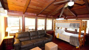 A wooden cabin with a sofa, ottoman, bunk bed, and a ceiling fan. - Deer Hollow Cabin - A family-friendly 3-bedroom cabin in charming Three Rivers (Three Rivers)