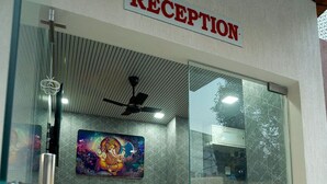 A reception area with a glass door, two orange chairs, a ceiling fan, and a painting of a deity on the wall.