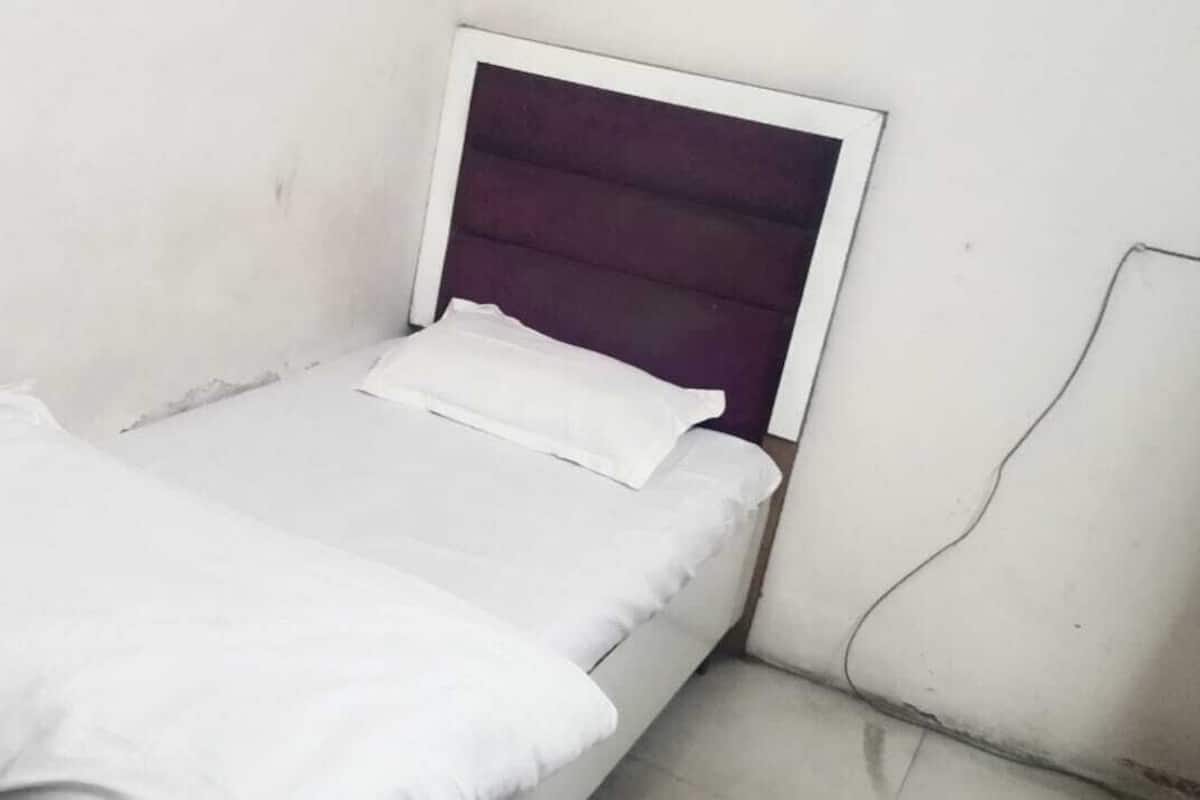 A small, single-bed room with a white bedspread and a purple headboard.
