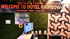 Ein Empfangsschalter mit einem Computermonitor, einem Telefon und einem Schild mit dem Hotelnamen und der Angabe zur Check-out-Zeit.