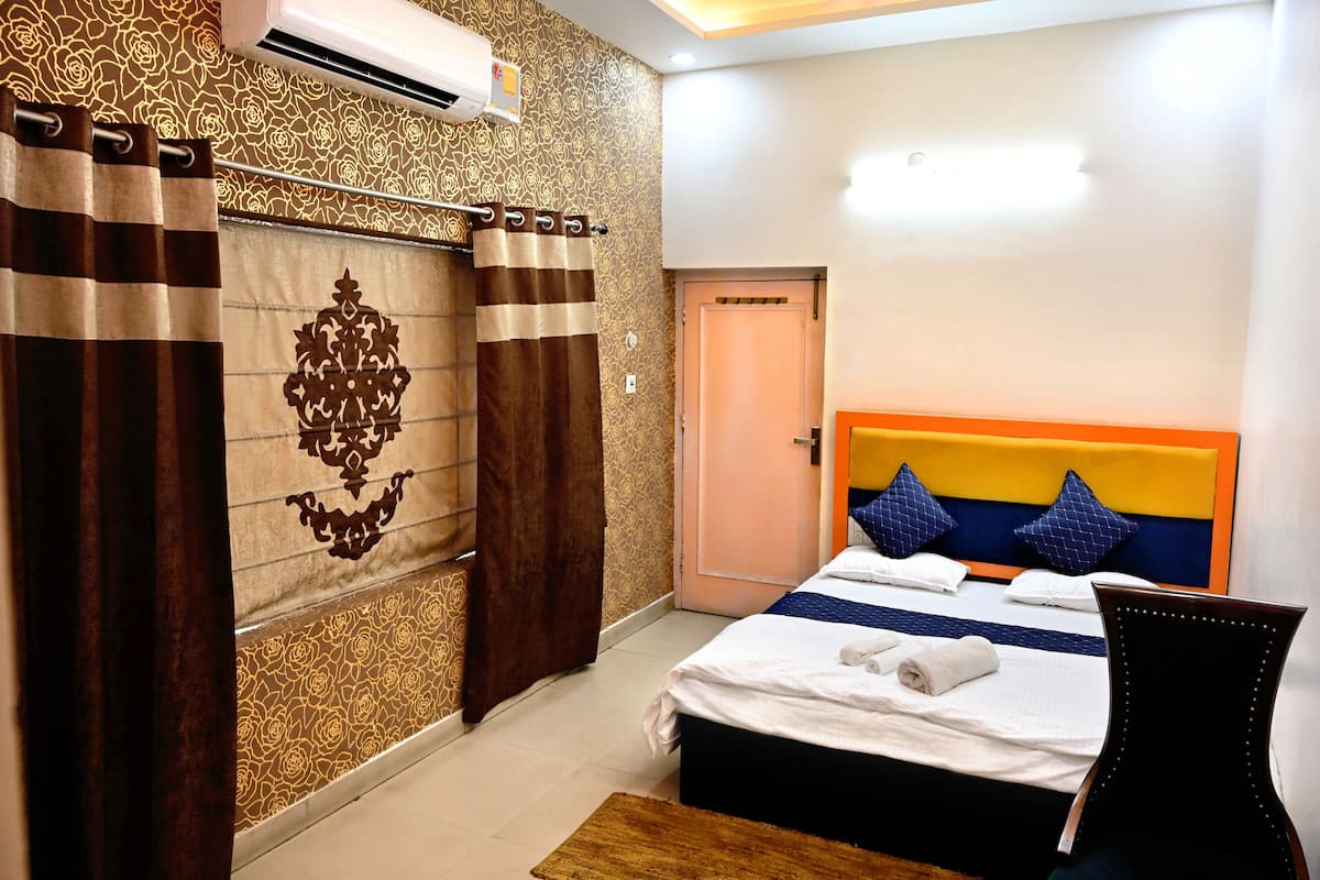 A hotel room with a bed, a chair, a door, and an air conditioning unit.