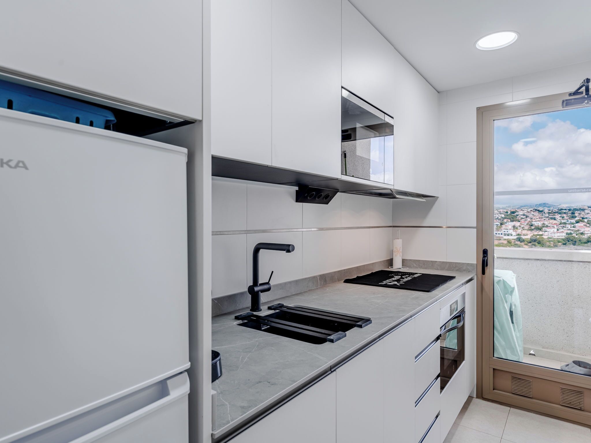 Uma cozinha moderna com forno embutido, pia e janela com vista para a cidade.
