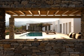 Un espace piscine extérieur moderne, agrémenté de murs en pierre, d’une pergola en bois et de chaises longues.
