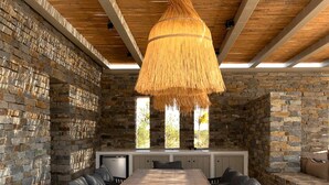 Un comedor rústico con una larga mesa de madera, sillas tapizadas en negro y una lámpara de techo de fibra trenzada.
