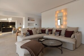 Un salon moderne avec un canapé d’angle, une table basse ronde et un grand miroir avec éclairage intégré.