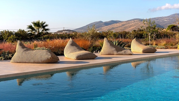Zona junto a la piscina con cuatro pufs de mimbre y vistas despejadas a las montañas.