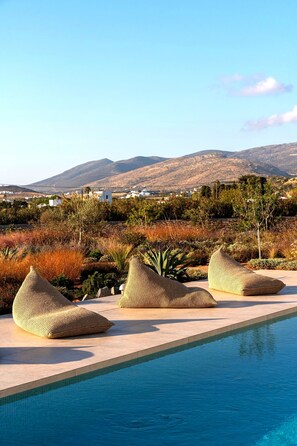 Un espace piscine agrémenté de trois poufs en tissu tressé, avec une vue sur les montagnes et les bâtiments en arrière-plan.