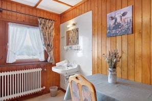 L’intérieur d’une cabine, avec un revêtement mural en bois, une fenêtre avec des rideaux, un lavabo, un miroir, une table sur laquelle est posé un vase, et un tableau accroché au mur.