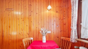 Ein Zimmer mit Holzvertäfelung, ausgestattet mit einem Tisch, Stühlen, einer Vase mit getrockneten Blumen, einer Lampe und einem Heizkörper.