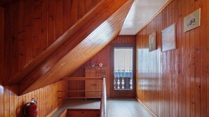Ein Holzinnenraum mit schrägverdeckter Decke, einem Feuerlöscher, einer Bank und einem Fenster mit Aussicht.