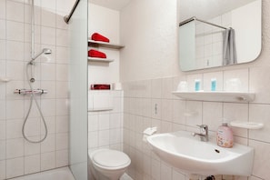 A bathroom with a shower, toilet, sink, and shelves with toiletries.